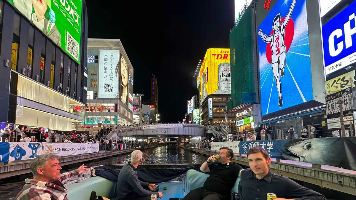 Neon signs reflected in the canal on a Dotonbori river cruise past the Glico sign, Osaka Japan