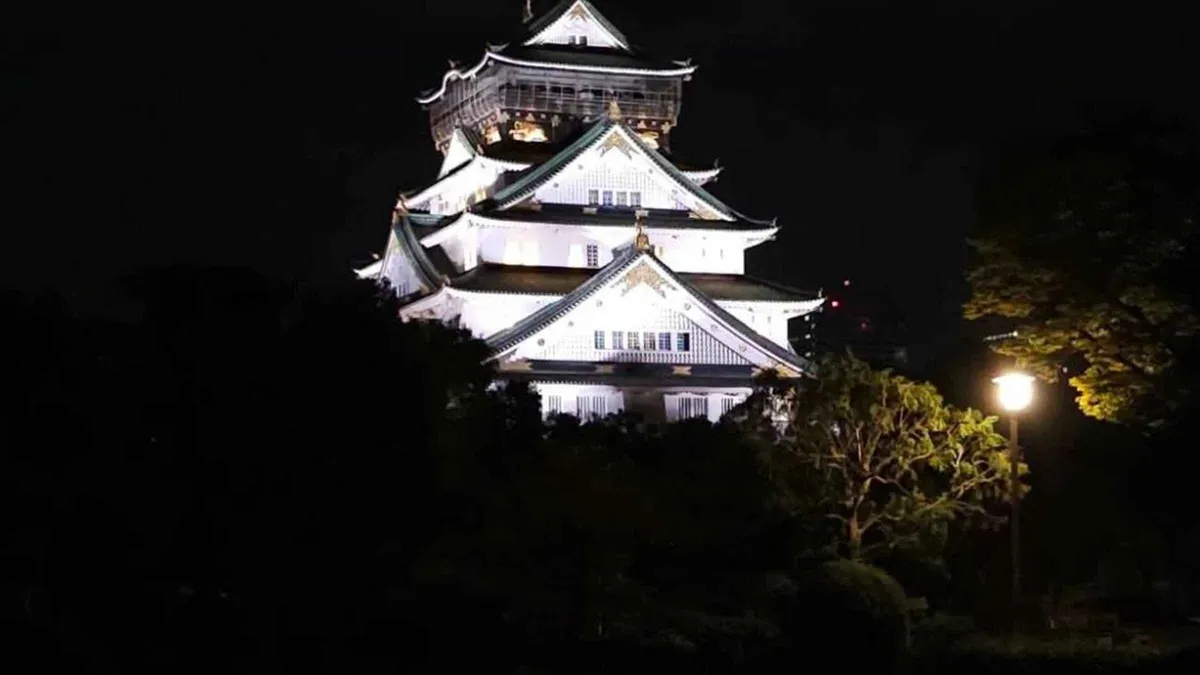 Guide telling ghost stories beside a lantern-lit gate on the Osaka Castle grounds at night, Osaka Japan