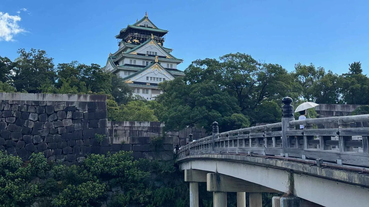 Visitor listening to an audio guide beside the moat on a self-guided Osaka Castle walking tour, Osaka Japan